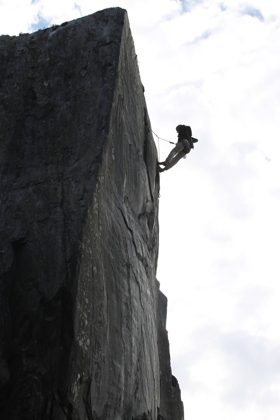 A climber silhouetted against a pale sky, high on the edge of a sheer slate wall